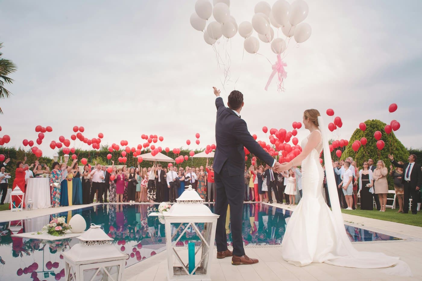 A couple from behind, holding hands, balloons rising.