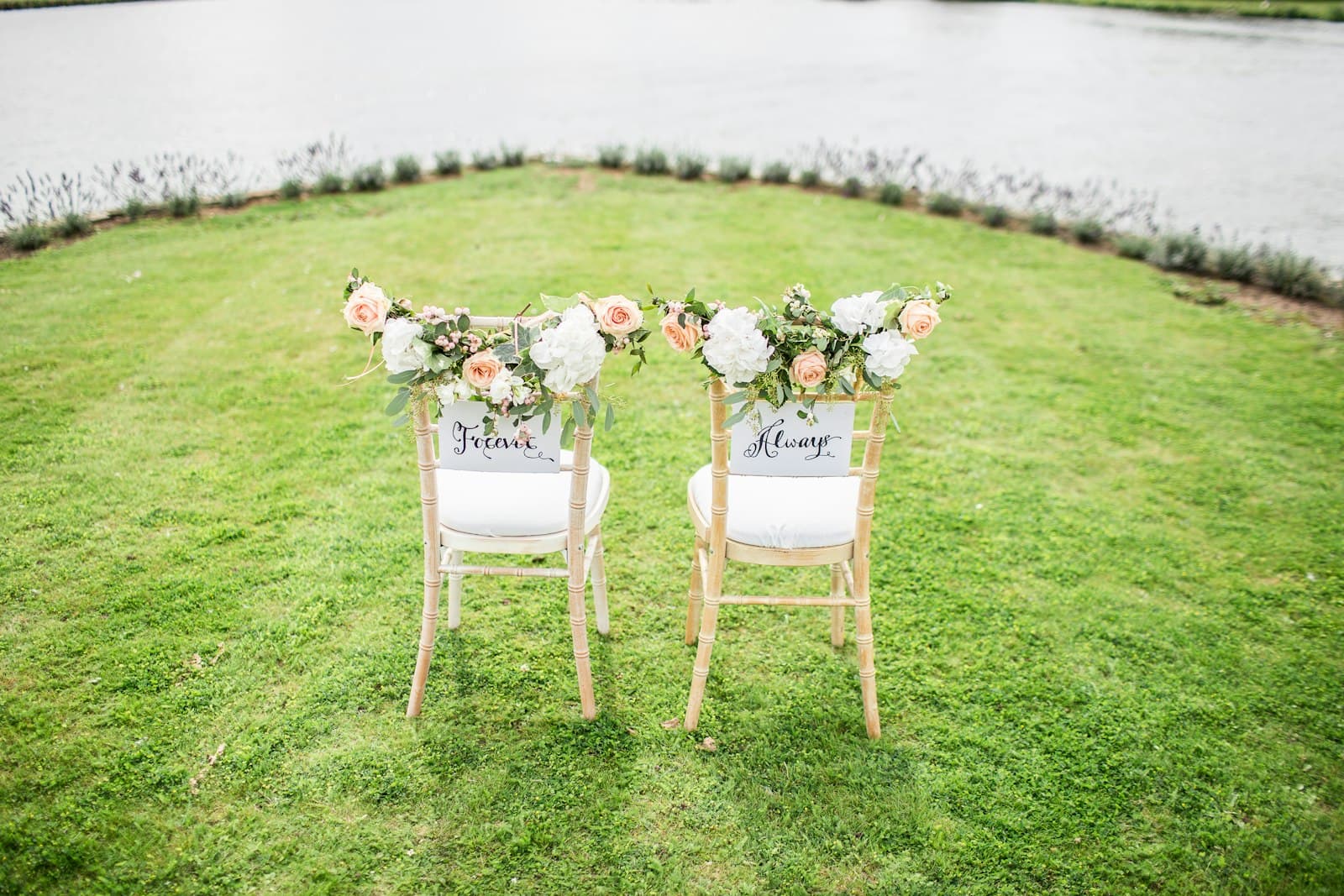 Two chairs by the water, with flowers and a name on each.